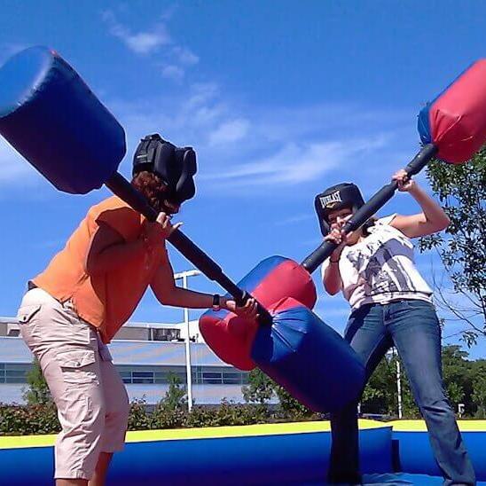 2 people on blue inflatable fighting with huge inflatable bars in gladiator joust team building event