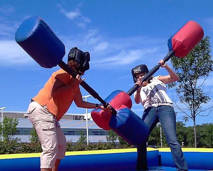 2 people on blue inflatable fighting with huge inflatable bars in gladiator joust team building event