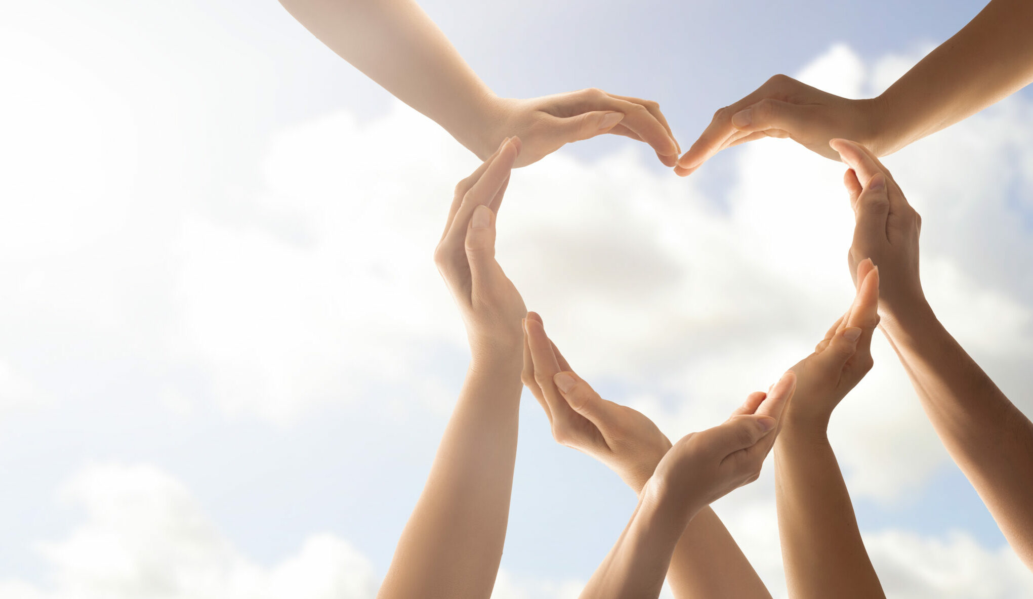 Group of people creating a heart out of hands in the sky
