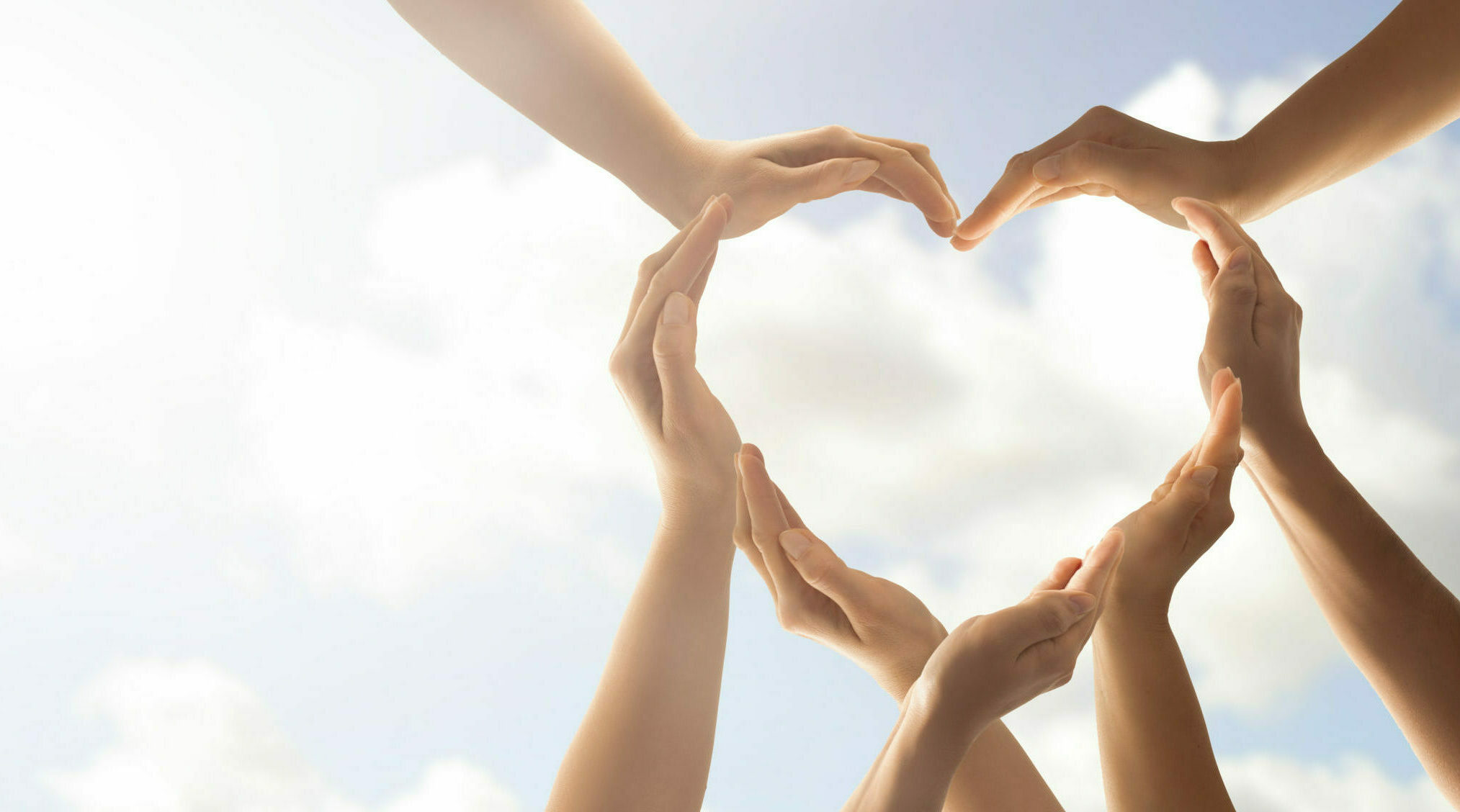 Group of people creating a heart out of hands in the sky