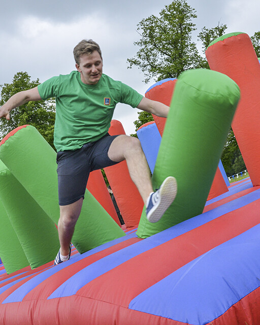 Man jumping on colourful inflatable assault course in outdoor summer team building event