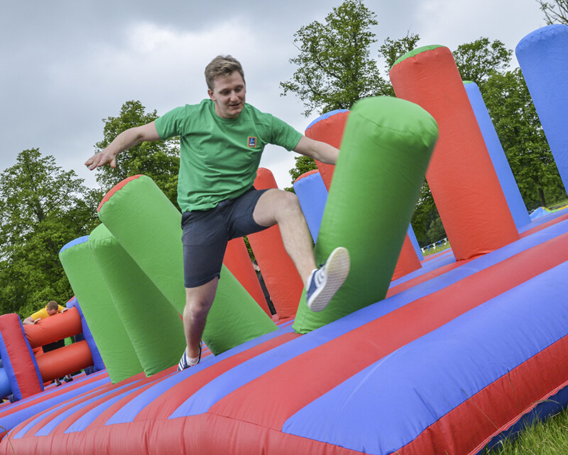 Man jumping on colourful inflatable assault course in outdoor summer team building event