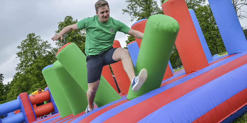 Man jumping on colourful inflatable assault course in outdoor summer team building event