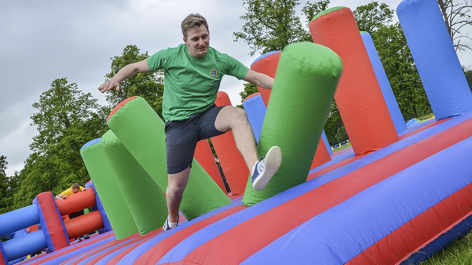 Man jumping on colourful inflatable assault course in outdoor summer team building event