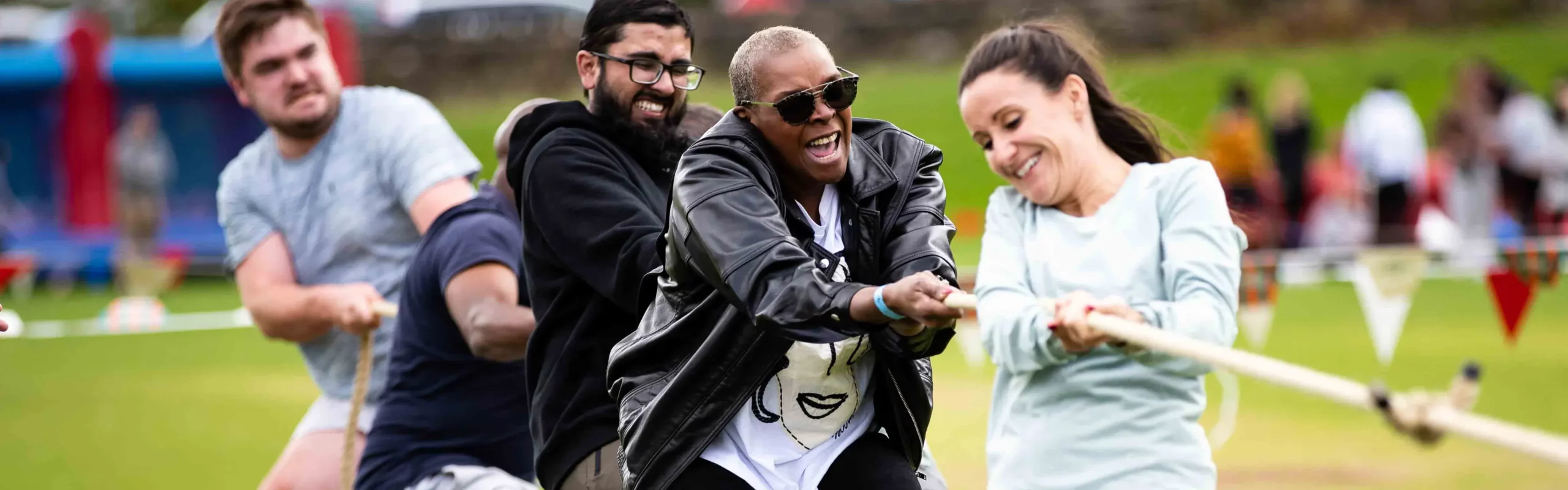 Outdoor team building Olympics-themed tug of war with happy people pulling on rope