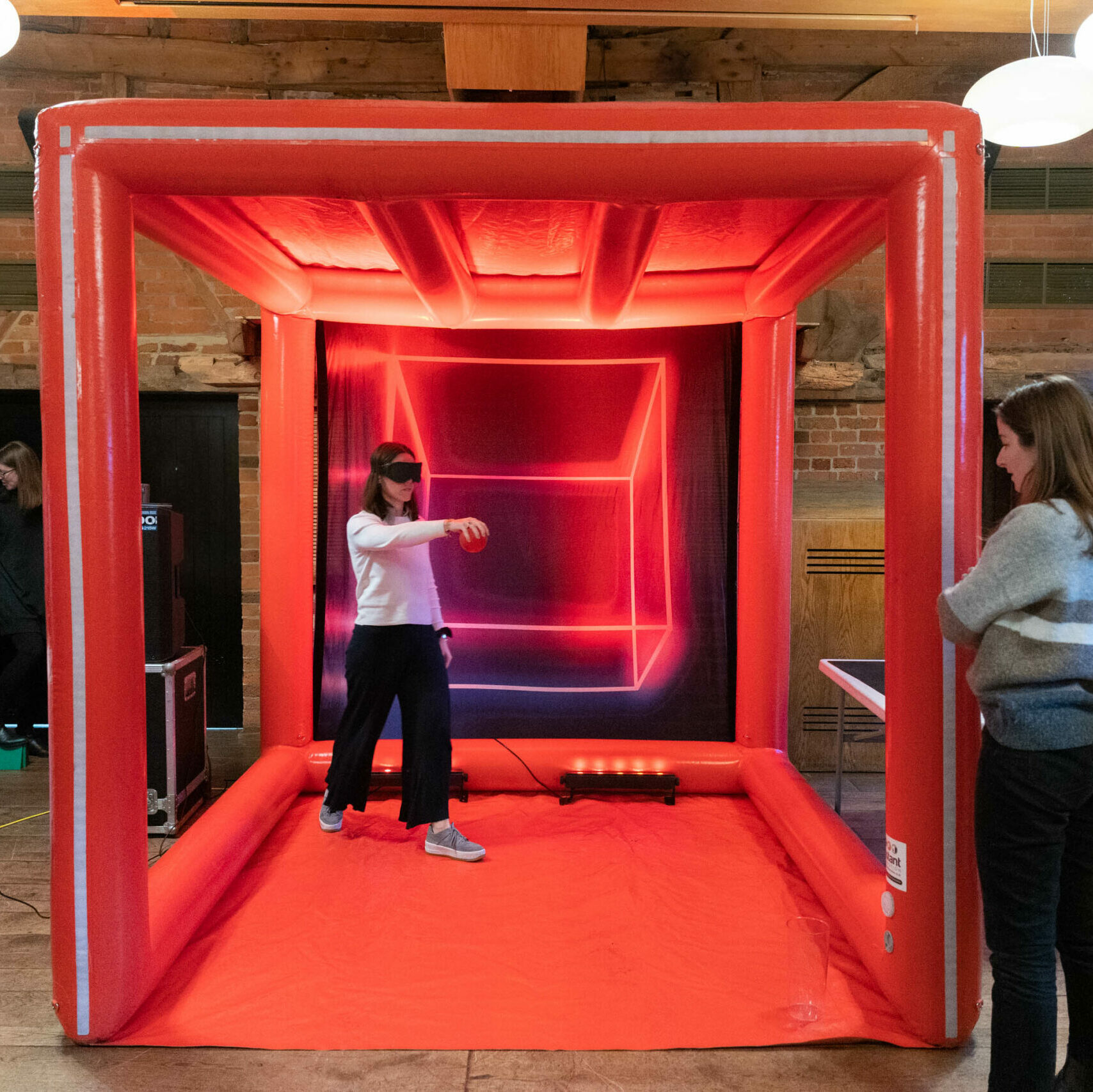 A women playing the ball drop game inside a giant red inflatable cube.