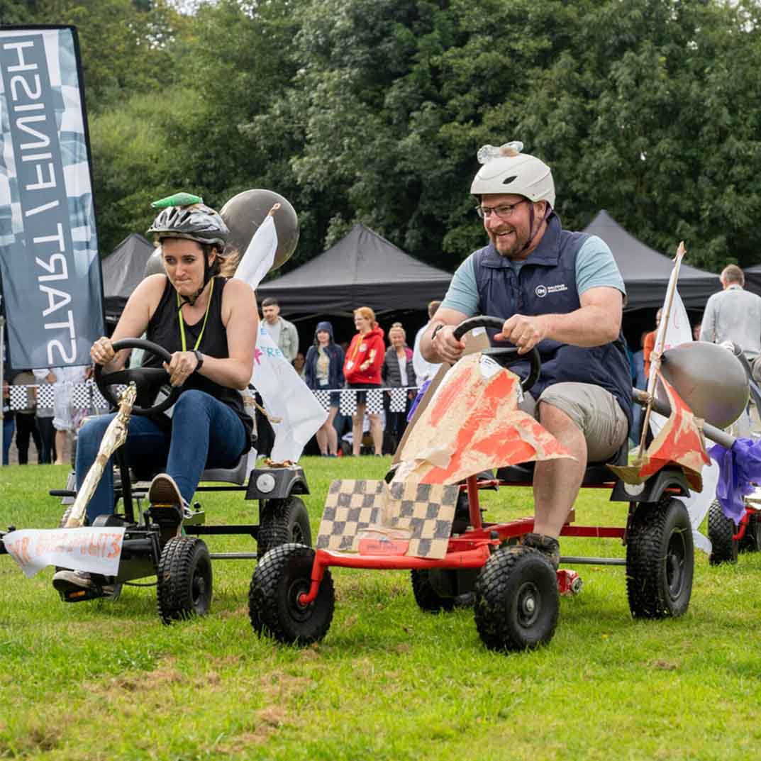 Two people on pedal power go karts racing on a field