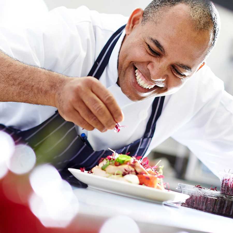Chef sprinking the finishing garnish onto a plate of food