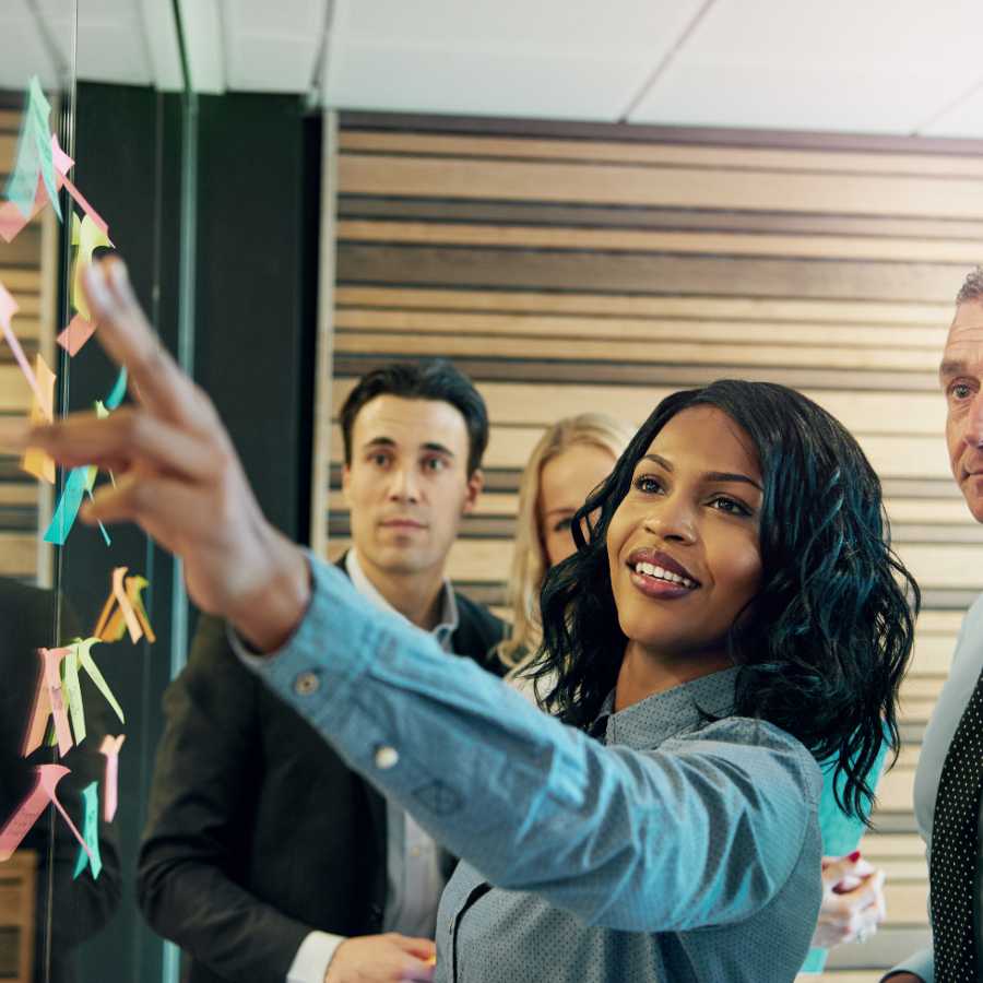 Lady leading a team pointing to post-it notes on a screen